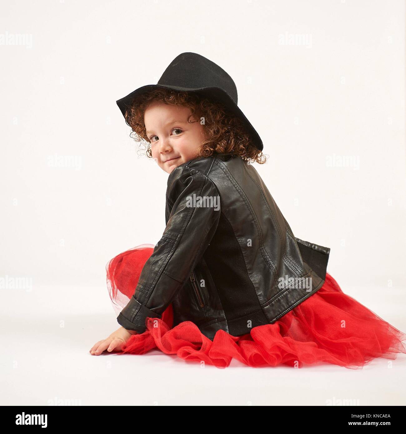 Kleines Mädchen mit schwarzen Hut sitzt und lächelt. Stockfoto