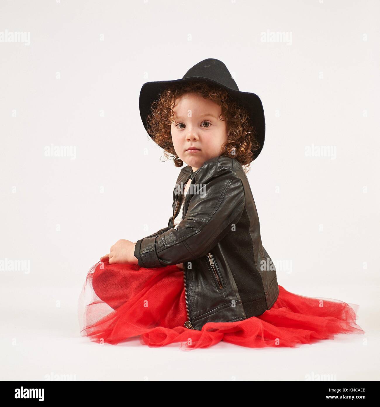 Kleines Mädchen mit schwarzen Hut sitzt und schaut. Stockfoto