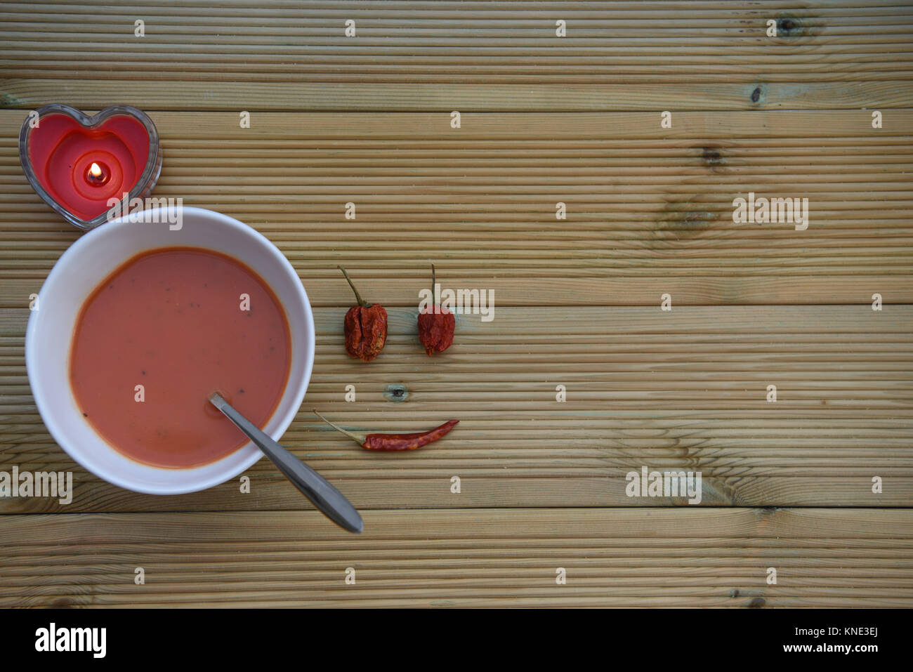 Gesundes Essen Fotografie Bild von hausgemachten Tomate Basilikum Suppe in weiße Schüssel mit Löffel und Rote Liebe Herz Form Kerze auf rustikalem Holz mit Platz Stockfoto