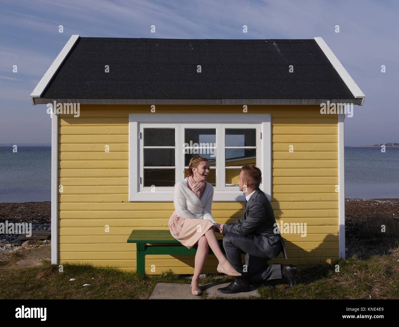Nahaufnahme eines attraktiven jungen Paares am Strand vor einer niedlichen gelben Strandhütte an einem windigen Wintertag, der sich gegenseitig in die Augen schaut Stockfoto
