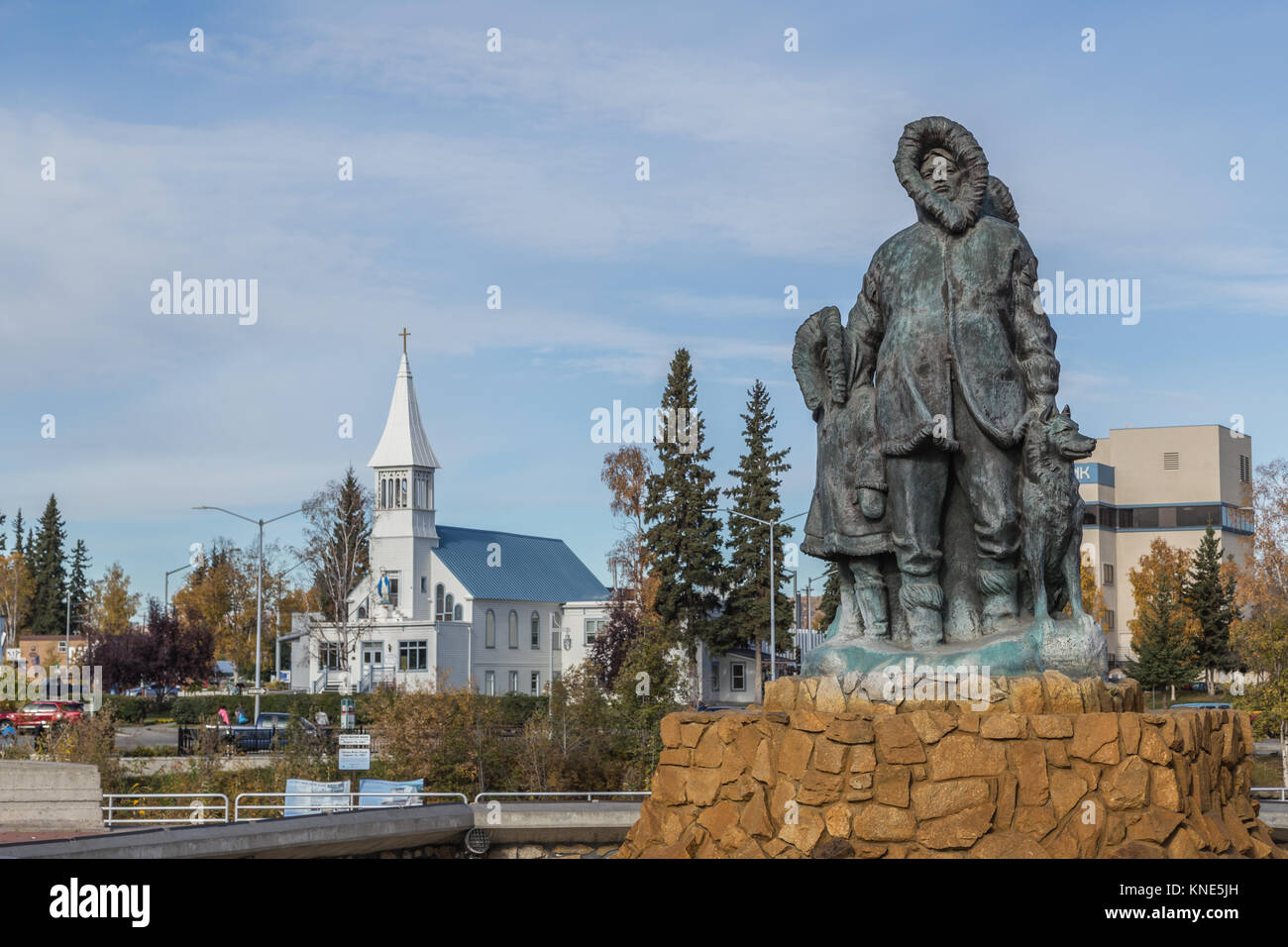 Unbekannte erste Familie Statue im goldenen Herzen Park in der Innenstadt von Fairbanks, Alaska, USA im Herbst mit der Unbefleckten Empfängnis Katholische Kirche Stockfoto