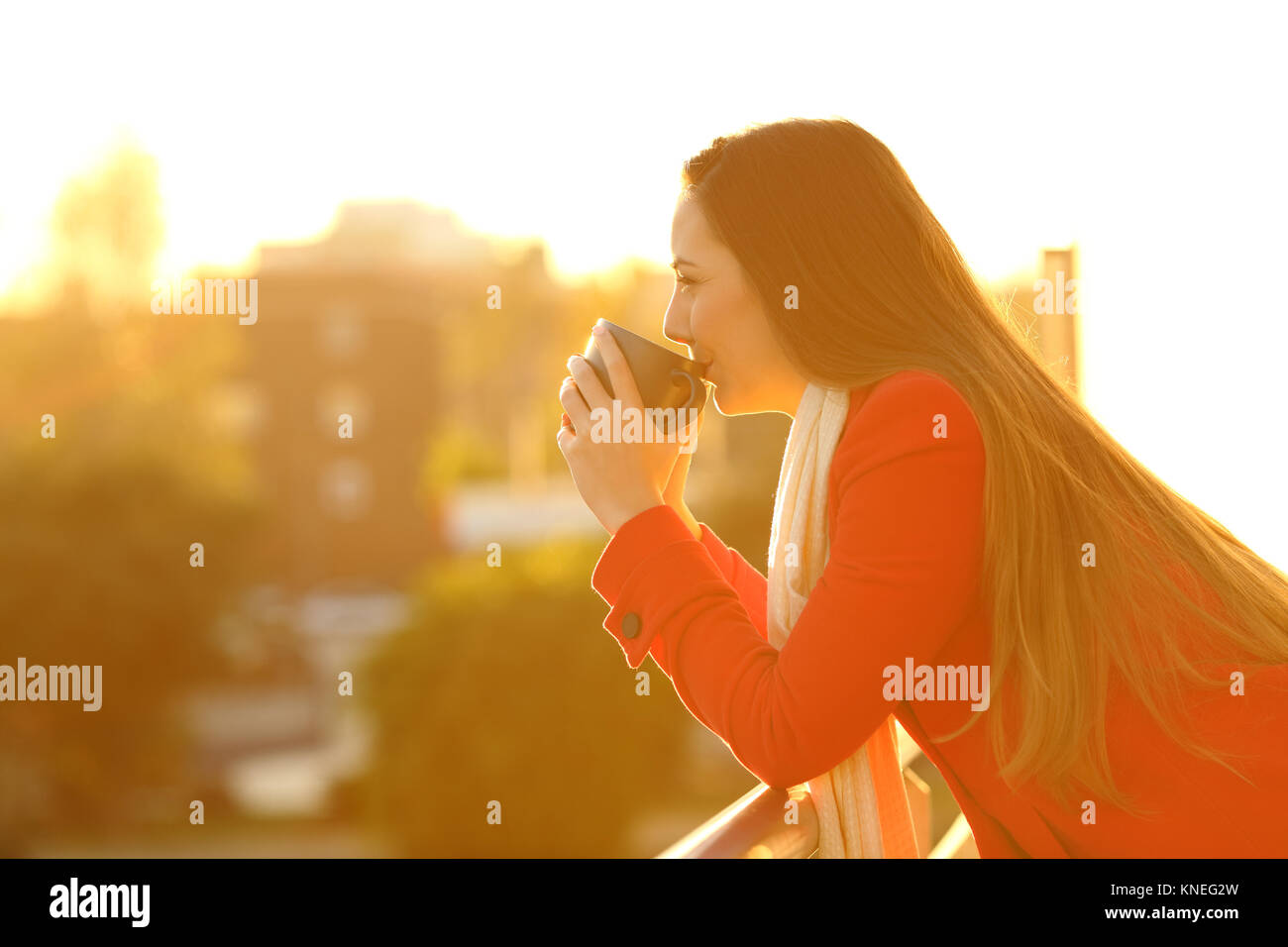 Seitenansicht Portrait von eine nachdenkliche Frau einen roten Mantel trinken Kaffee draußen tragen in einem Haus Balkon im Winter Stockfoto