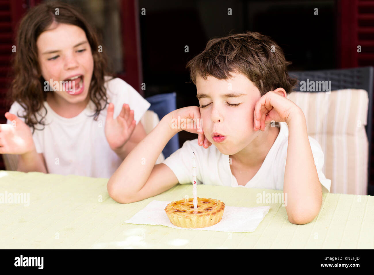 Junge Ausblasen Geburtstag Kerze, seine Schwester neben ihm sitzen Klatschen Stockfoto