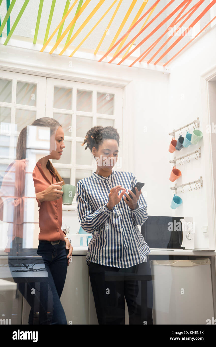 Zwei Unternehmerinnen auf Smartphone während einer Kaffeepause im Büro Küche Stockfoto