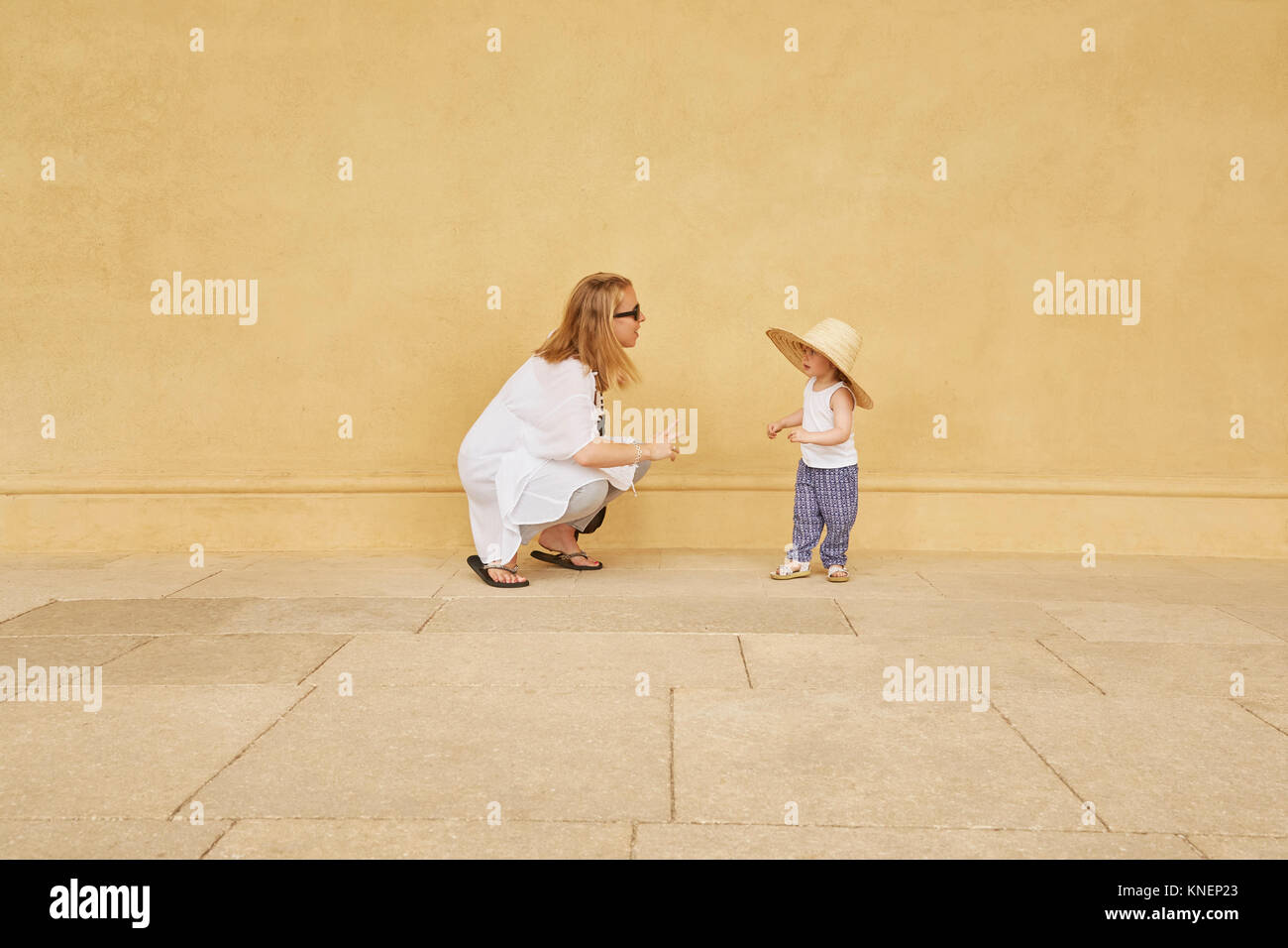 Schwangere Frau und Tochter spielen durch gelbe Wand Stockfoto