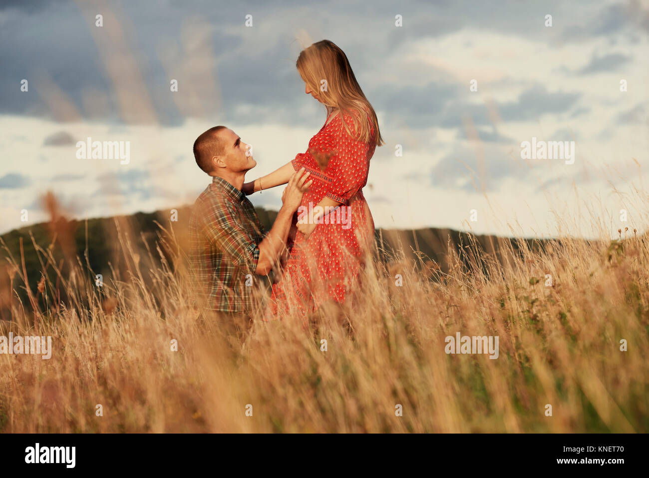 Mitte der erwachsene Mann kniend mit Hand auf die schwangere Frau Magen im Feld Stockfoto