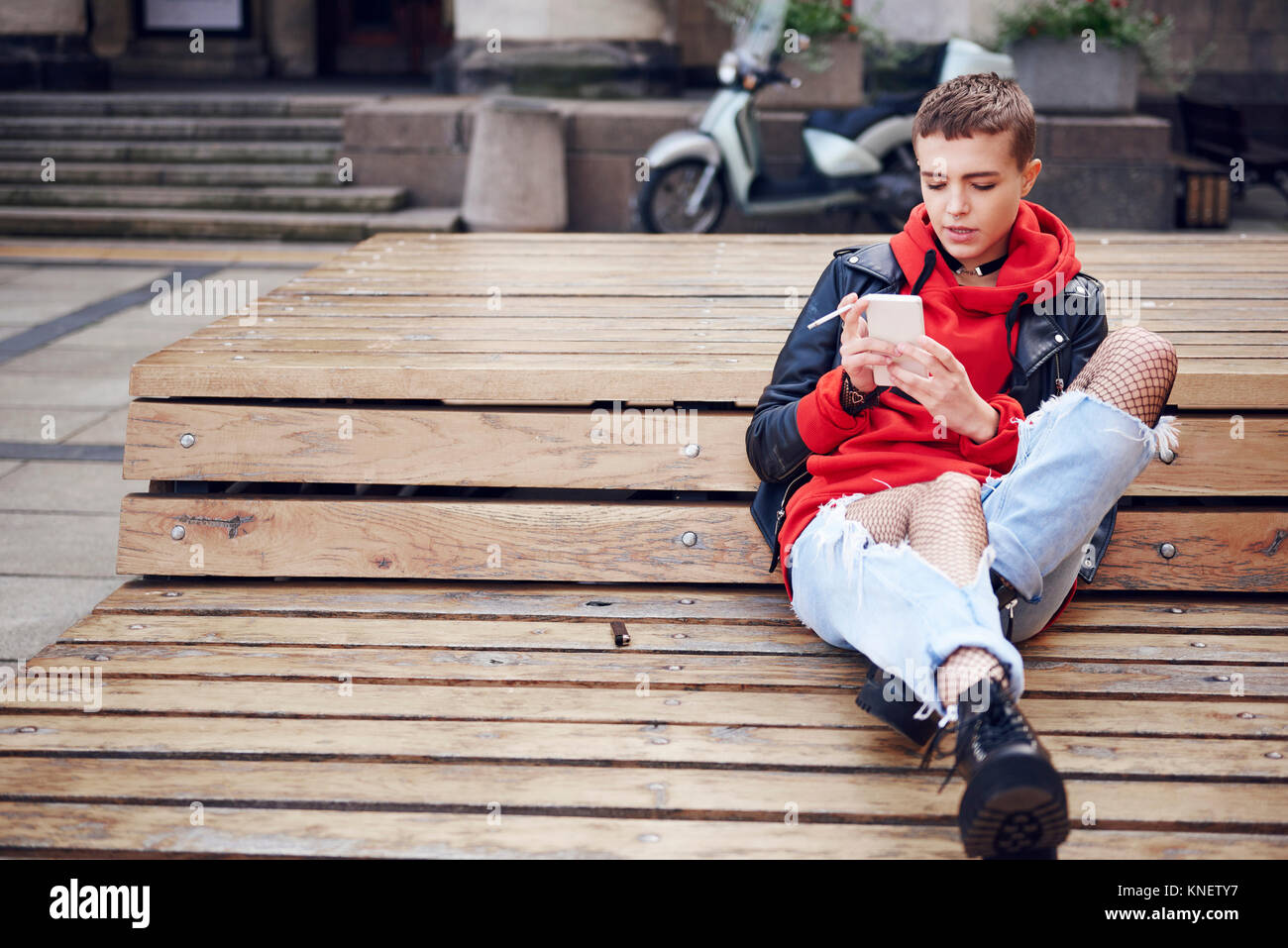 Cool junge Frau mit kurzen Haaren auf Smartphone und Rauchen Zigarette auf der City Bank suchen Stockfoto