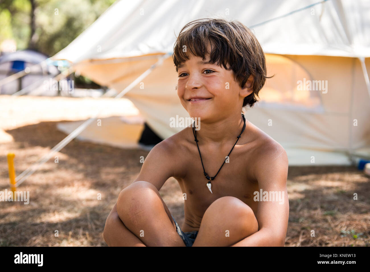 Happy bare chested Junge sitzt am Campingplatz Stockfoto