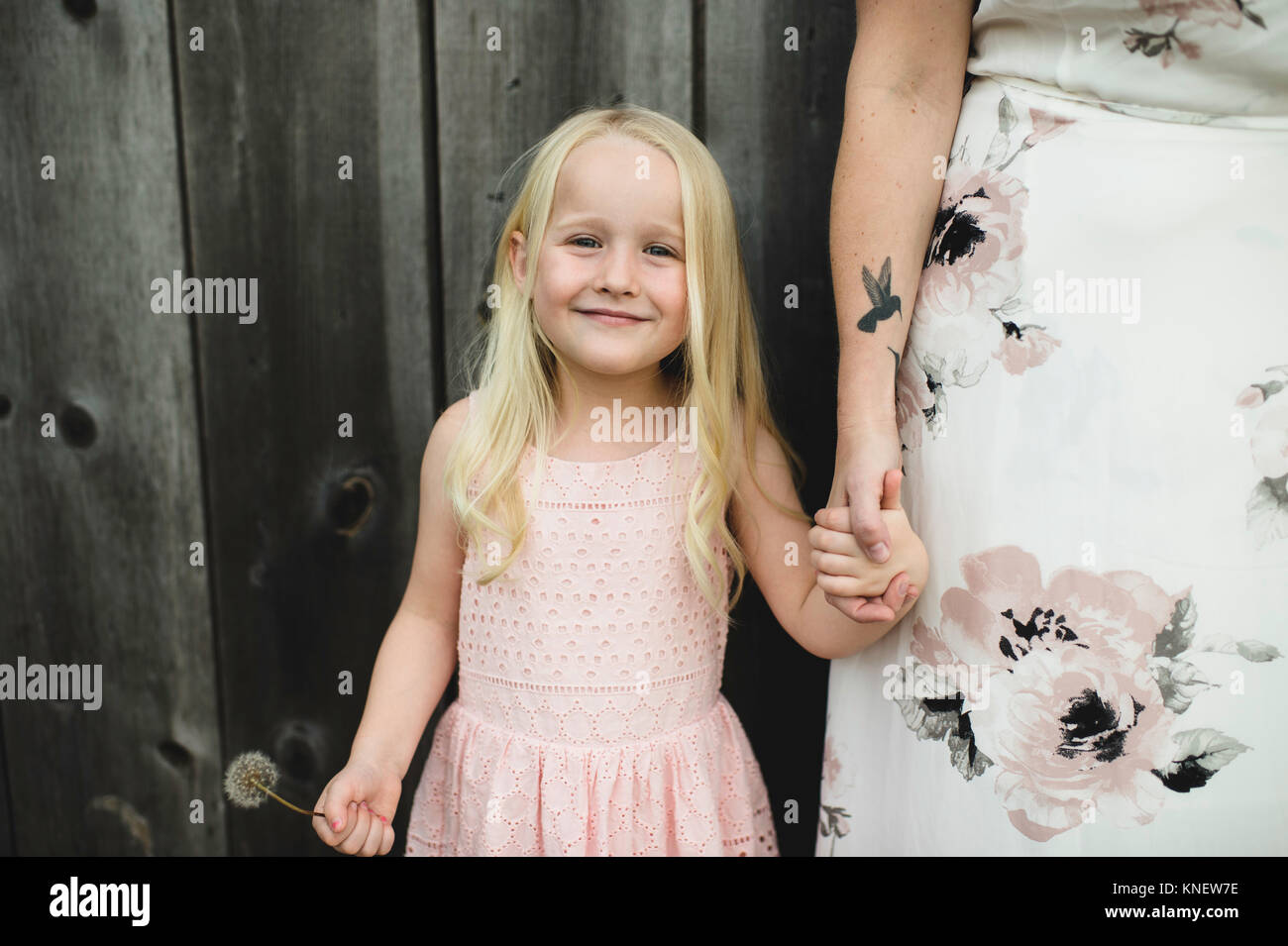 Portrait von Mädchen, dass Dandelion Clock und Mutter Hand an der Kamera schaut lächelnd Stockfoto