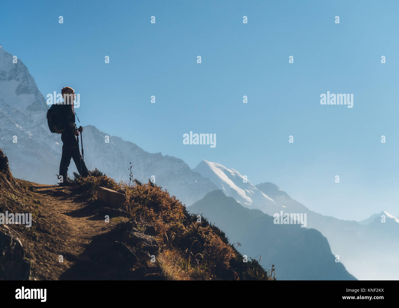 Stehende junge Frau mit Rucksack auf dem Hügel und Blick auf die Berge. Landschaft mit Mädchen, Pfad, Berge, blauer Himmel mit Wolken bei Sonnenaufgang in N Stockfoto