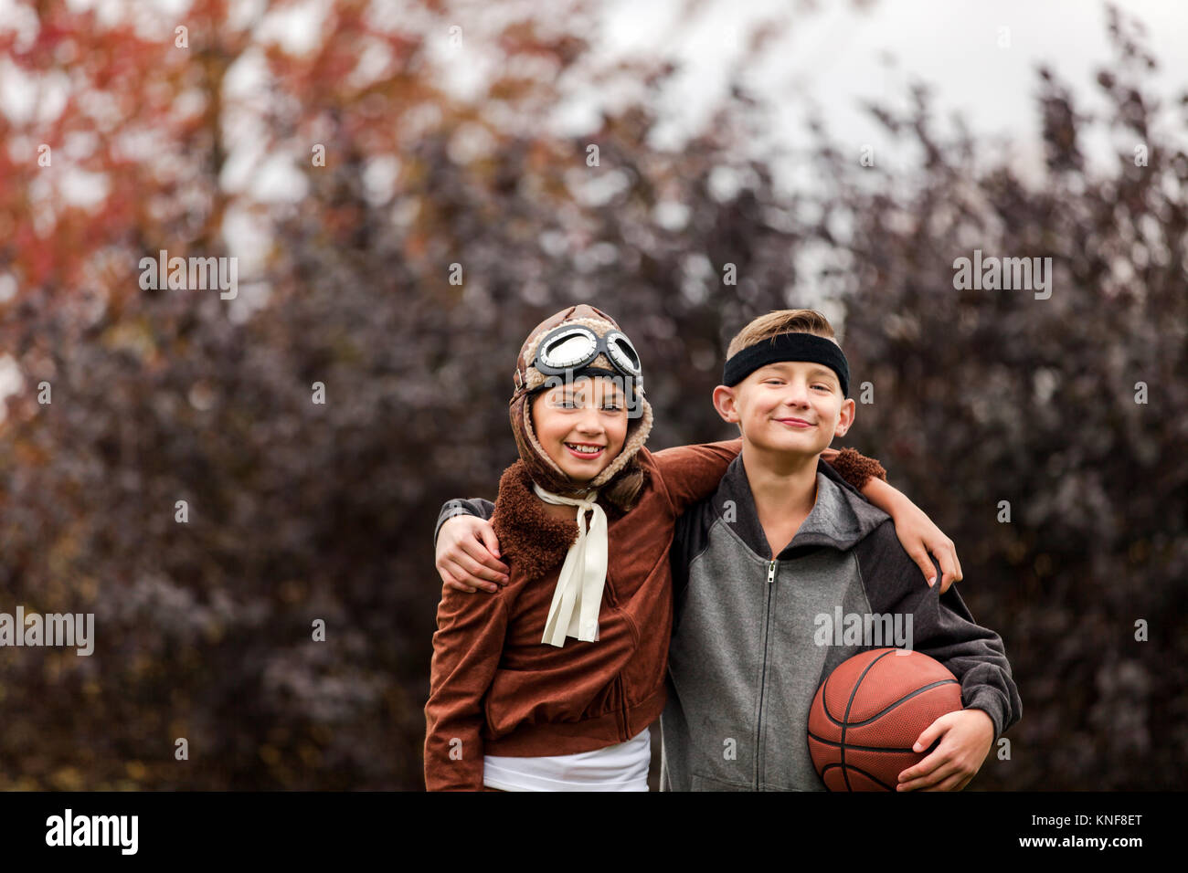 Porträt eines Mädchens und Zwillingsbruder tragen Basketballspieler und Pilot Kostüme für Halloween im Park Stockfoto