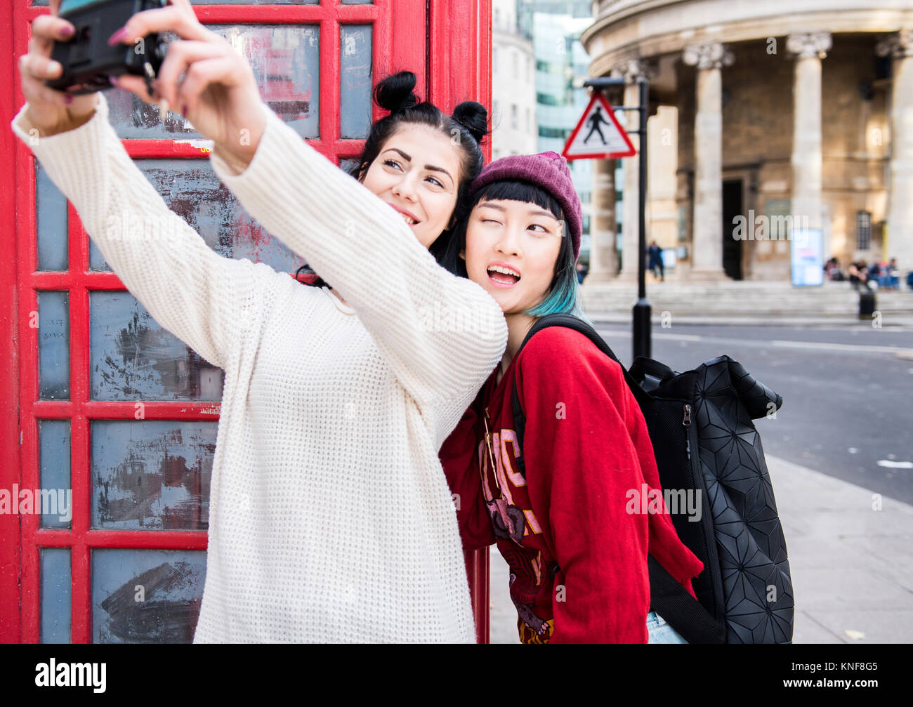 Zwei junge Frauen, die stilvollen selfie durch rote Telefonzelle, London, UK Stockfoto