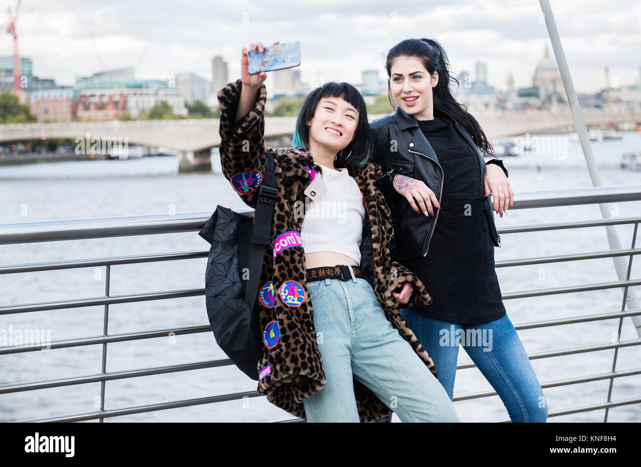 Zwei junge Frauen, die elegante Smartphone selfie auf Millennium Fußgängerbrücke, London, UK Stockfoto