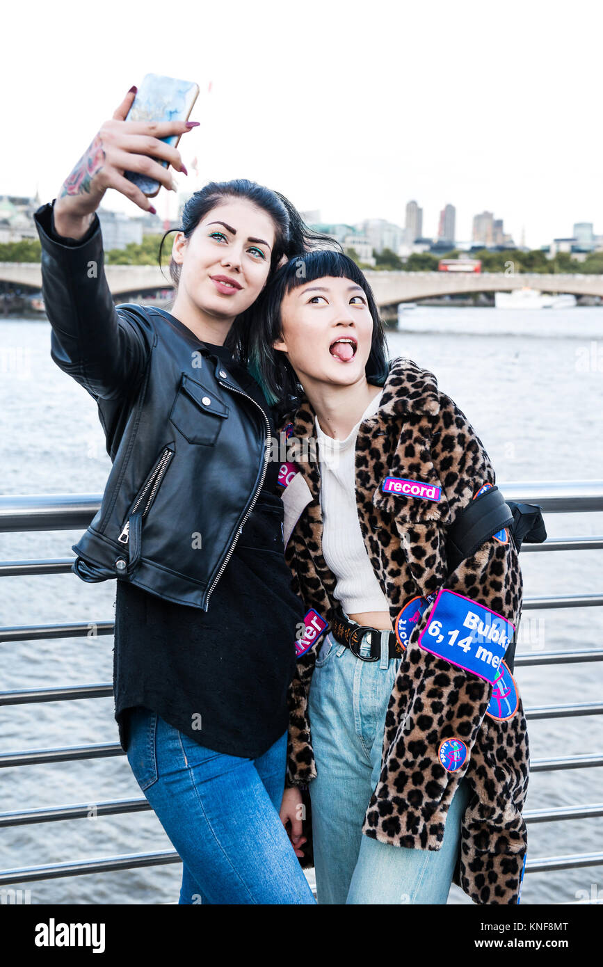 Zwei junge Frauen, die elegante Smartphone selfie auf Millennium Fußgängerbrücke, London, UK Stockfoto
