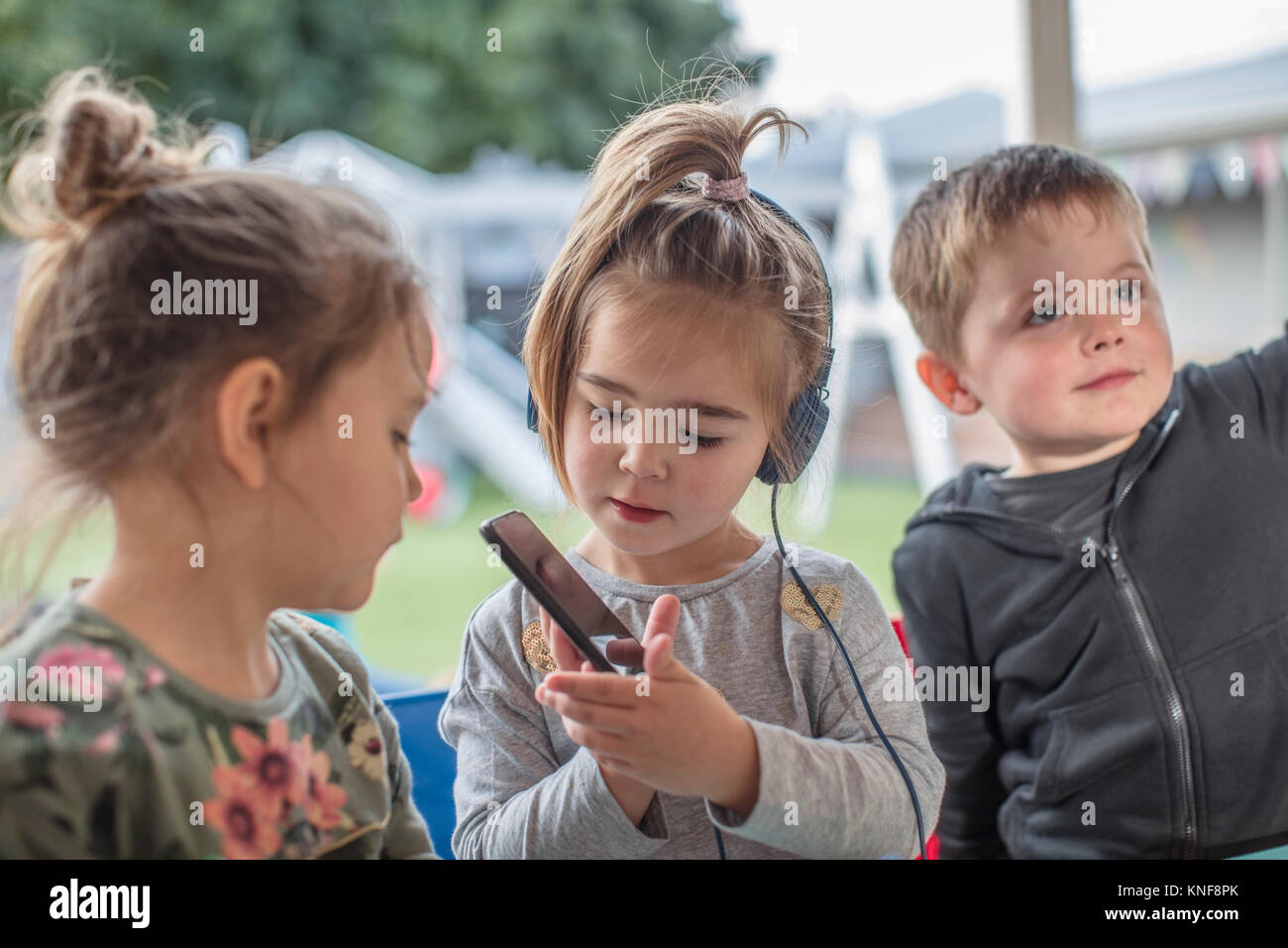 Junges Mädchen mit Freunden, mit Smartphone, das Tragen von Kopfhörern Stockfoto