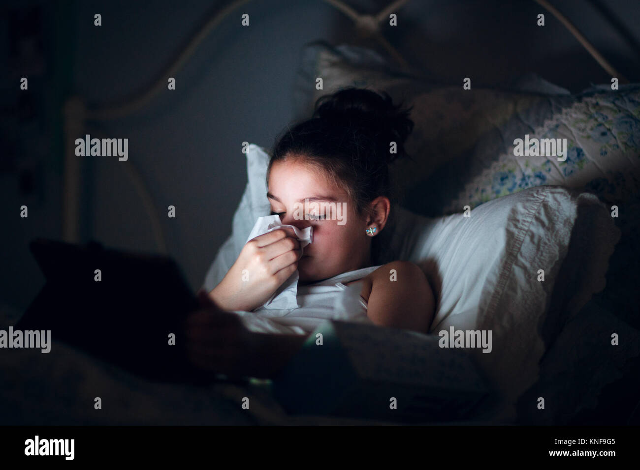 Mädchen im Bett blasen Nase, durch das Licht digital Tablet beleuchtet Stockfoto