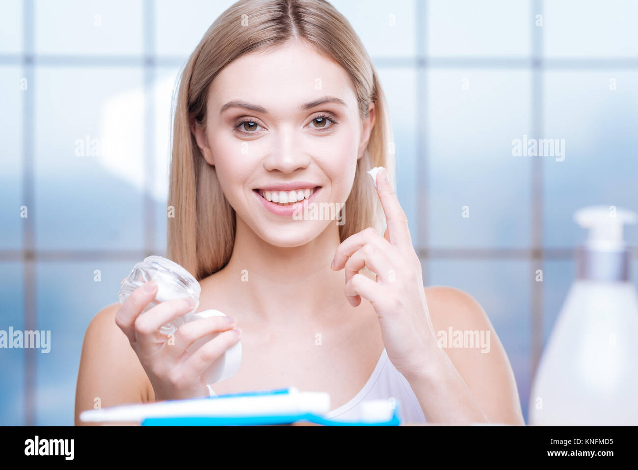 Lächelnde Frau über Creme zu ihrer Wange anzuwenden Stockfoto