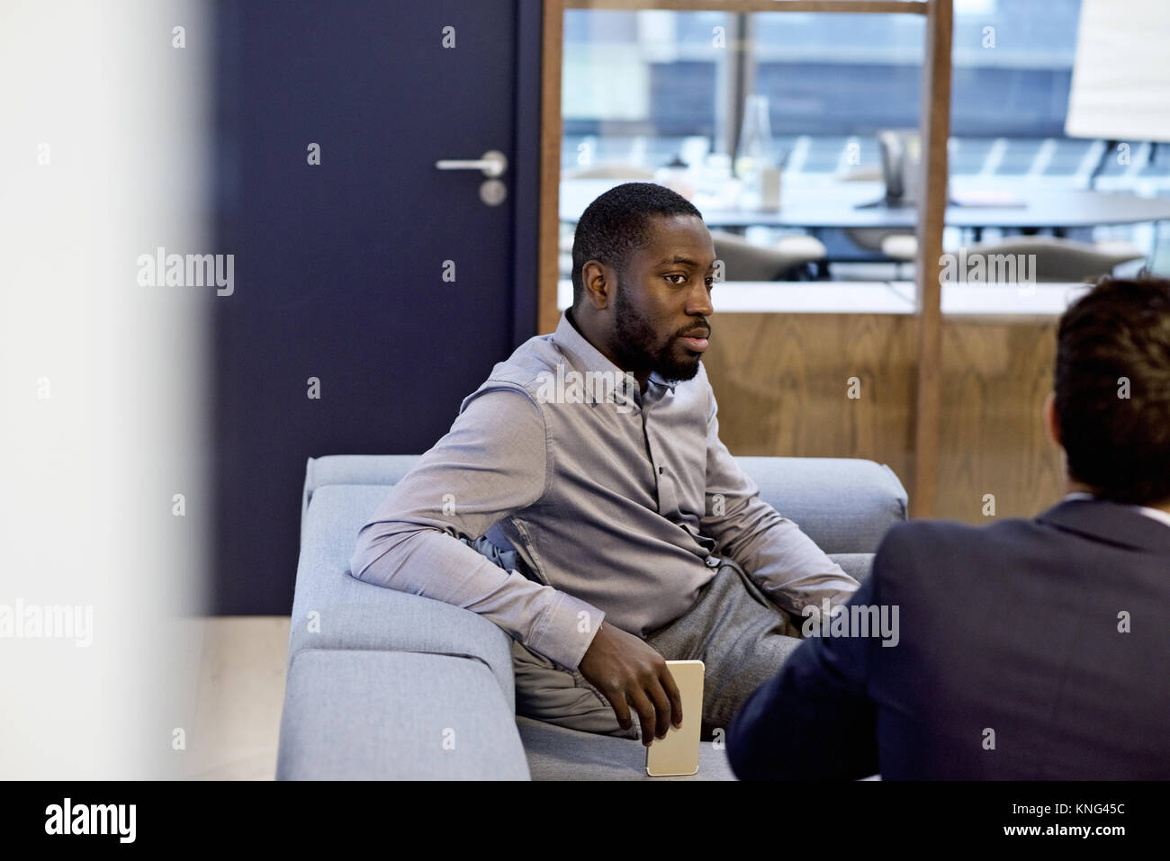Schwarzer Geschäftsmann gekleidet in einem smart Shirt im Gespräch mit Kollegen in einem modernen Interieur gestaltet Büro Stockfoto