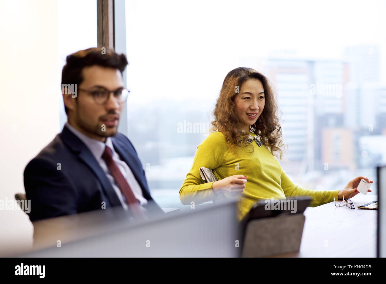 Asiatische Geschäftsfrau und kaukasischen Geschäftsmann an Ihrem Schreibtisch in einem hellen, modernen Großraumbüro bei Kollegen lächelnd vor der Kamera Stockfoto