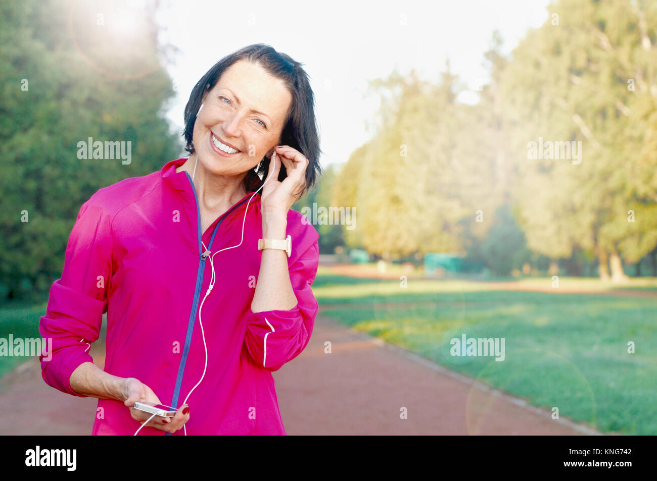 Reife Frau hören Musik vor oder nach dem Joggen im Park. Attraktive, reife Frau halten fit und gesund suchen Stockfoto