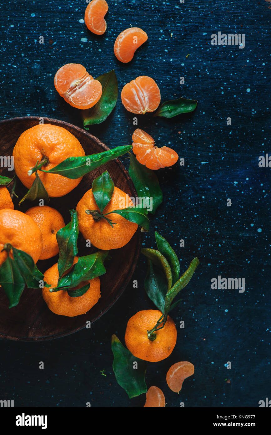 Zitrusfrüchte auf einer Holzplatte mit grünen Blättern. Lebendige Mandarinen auf einem dunklen Hintergrund. Rustikales essen Fotografie. Stockfoto