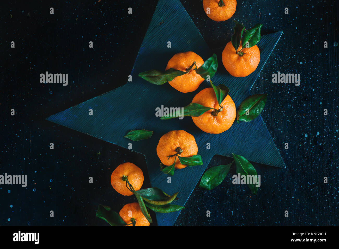Orange Mandarinen mit grünen Blättern auf einem sternförmigen Schneidebrett. Lebendige Früchte auf einem dunklen Hintergrund. Rustikales essen Fotografie. Stockfoto