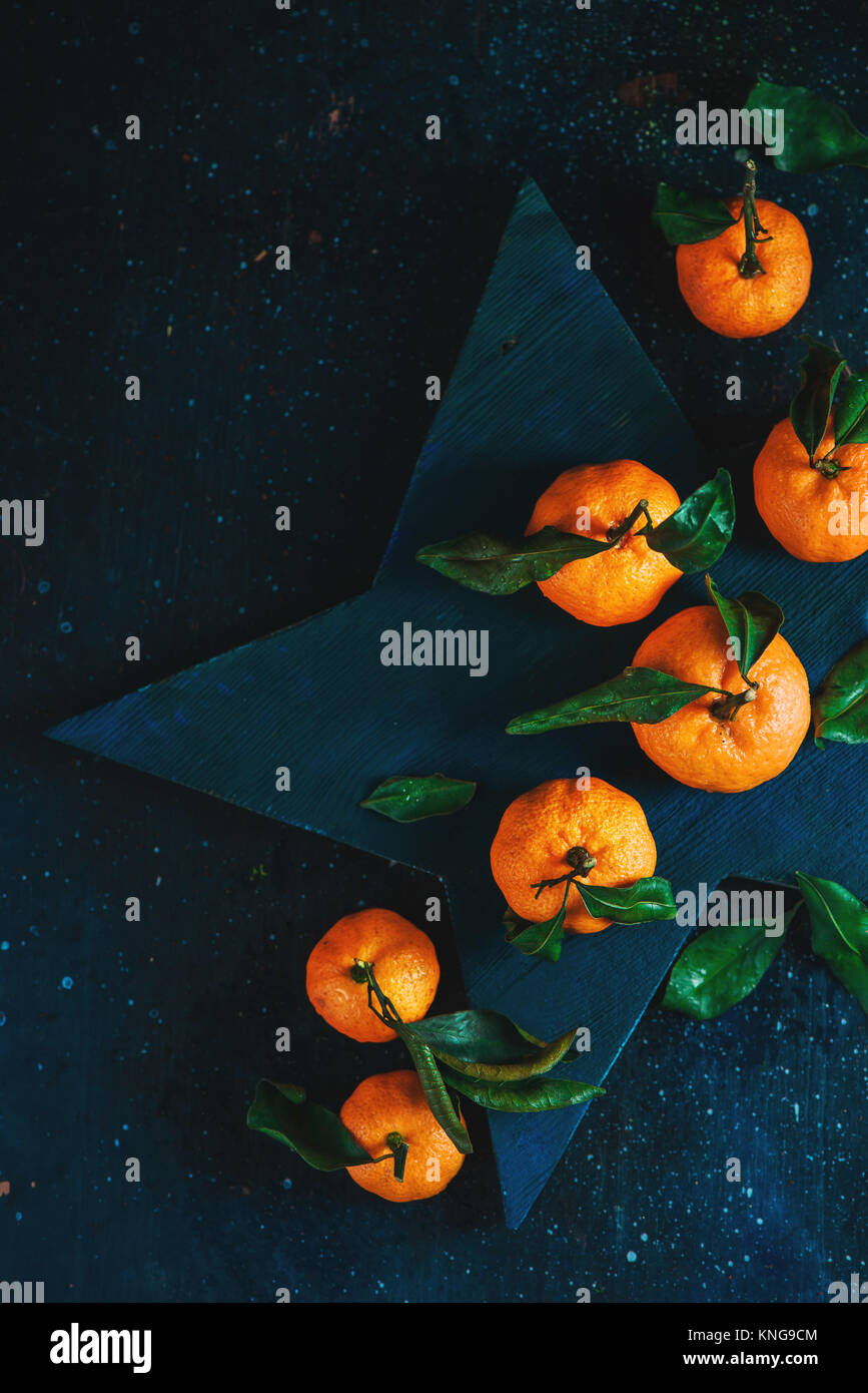 Orange Mandarinen mit grünen Blättern auf einem sternförmigen Schneidebrett. Lebendige Früchte auf einem dunklen Hintergrund. Rustikales essen Fotografie. Stockfoto