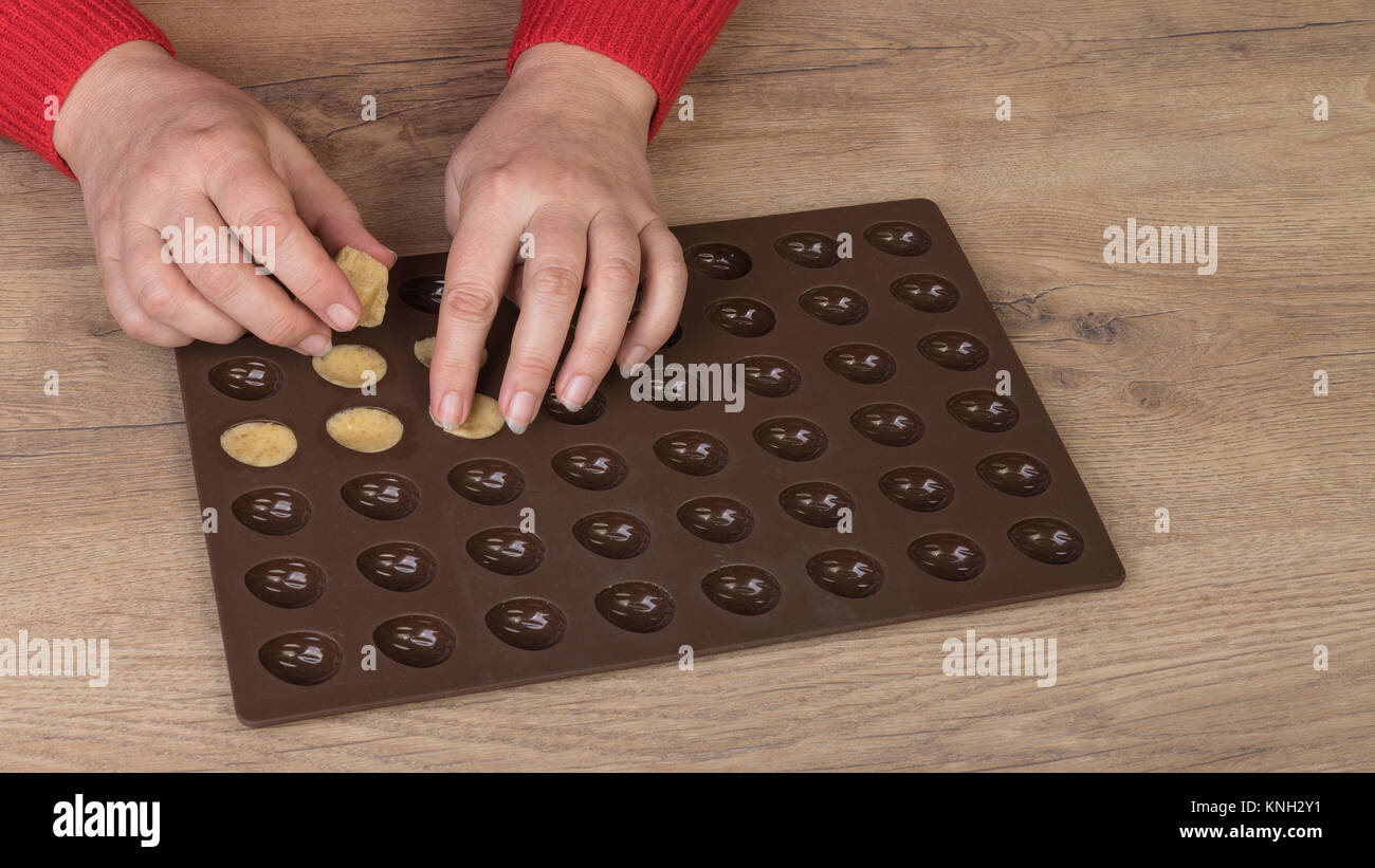 Die von Weihnachten Nüsse aus Mürbeteig verkneten. Weibliche Hände füllen ein Teig in Braun Silikonform mit Holz Hintergrund. Stockfoto