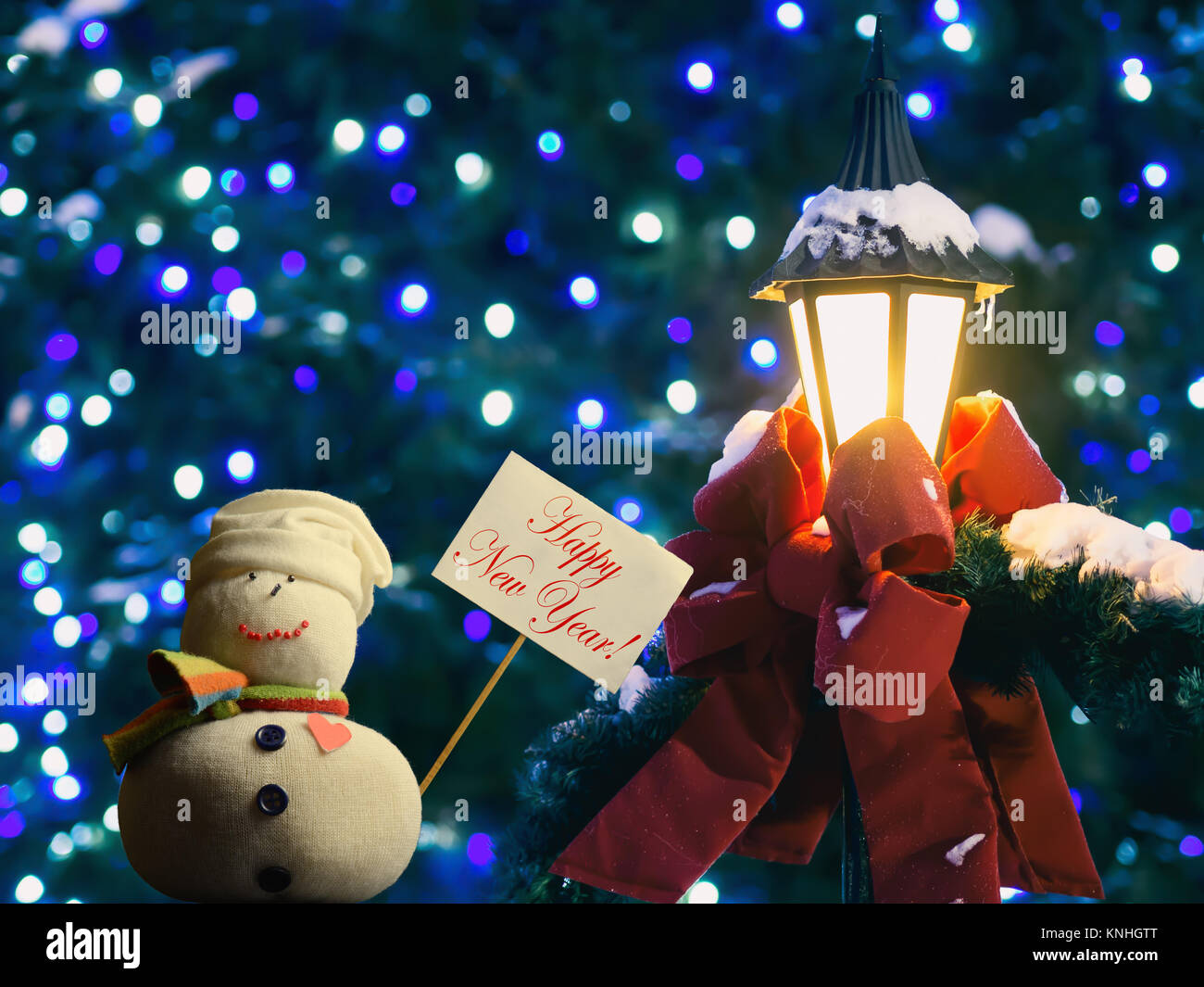 Schneemann Abbildung Holding ein Plakat mit Stock befestigt. Text "Frohes Neues Jahr!". Straßenlaterne in Red Ribbon und Tannenzweigen gewickelt. Stockfoto
