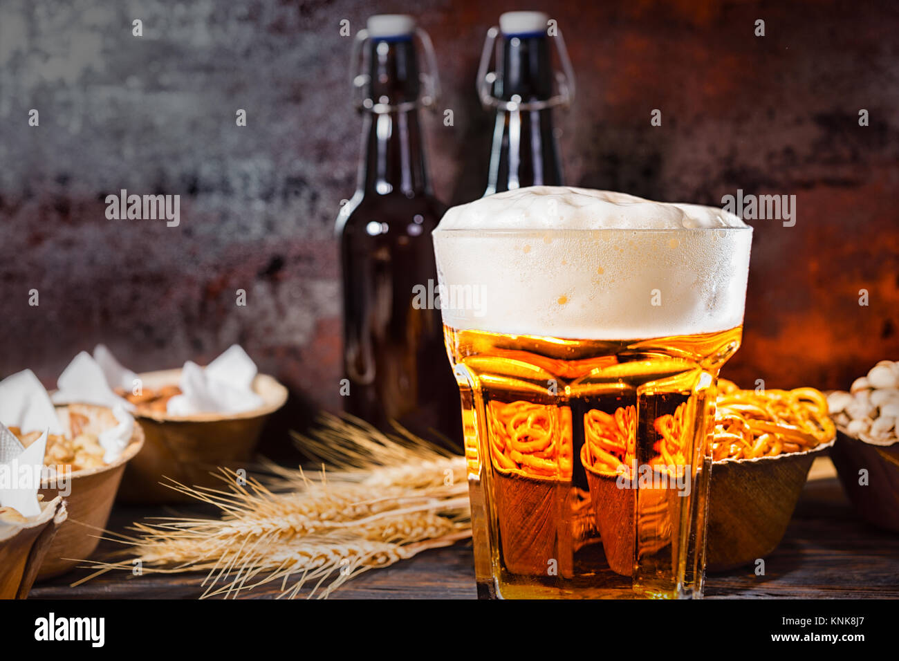 Glas mit frisch gezapften Bier und großem Kopf, der Schaum in der Nähe von  Flaschen, Weizen und die Platten mit den Snacks auf dunklem  Holzschreibtisch. Nahrungsmittel und Getränke Konzept Stockfotografie -  Alamy