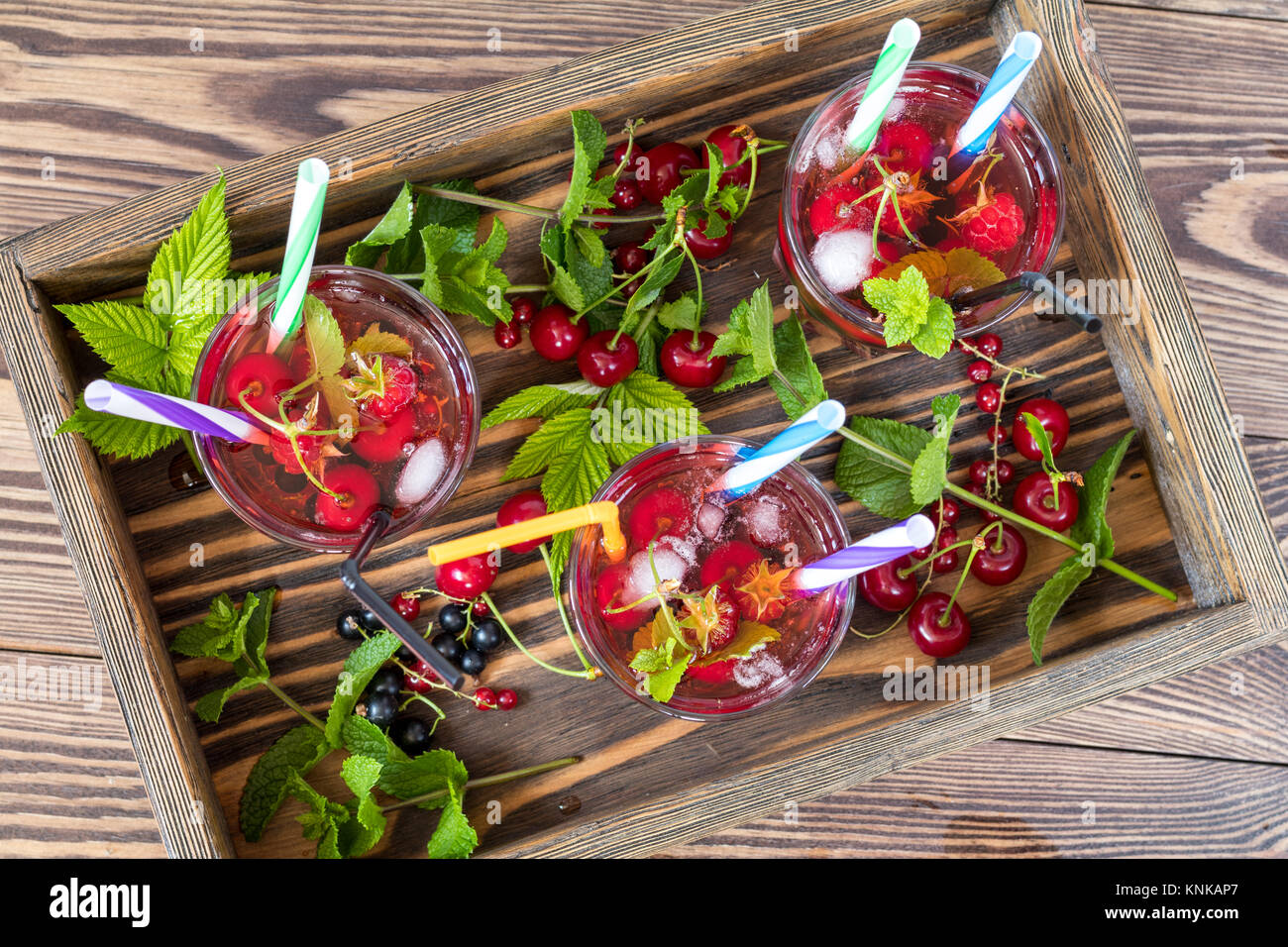 Drei Gläser erfrischenden Drink gewürzt mit frischem Obst im Holzkasten von Obst umgeben. Ansicht von oben. Holz- Hintergrund Stockfoto