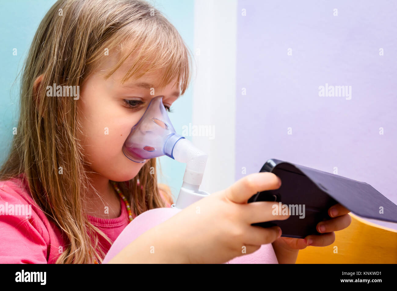 Kind ist die Inhalation mit Maske im Gesicht und Spiele mit Ihrem Telefon. Stockfoto