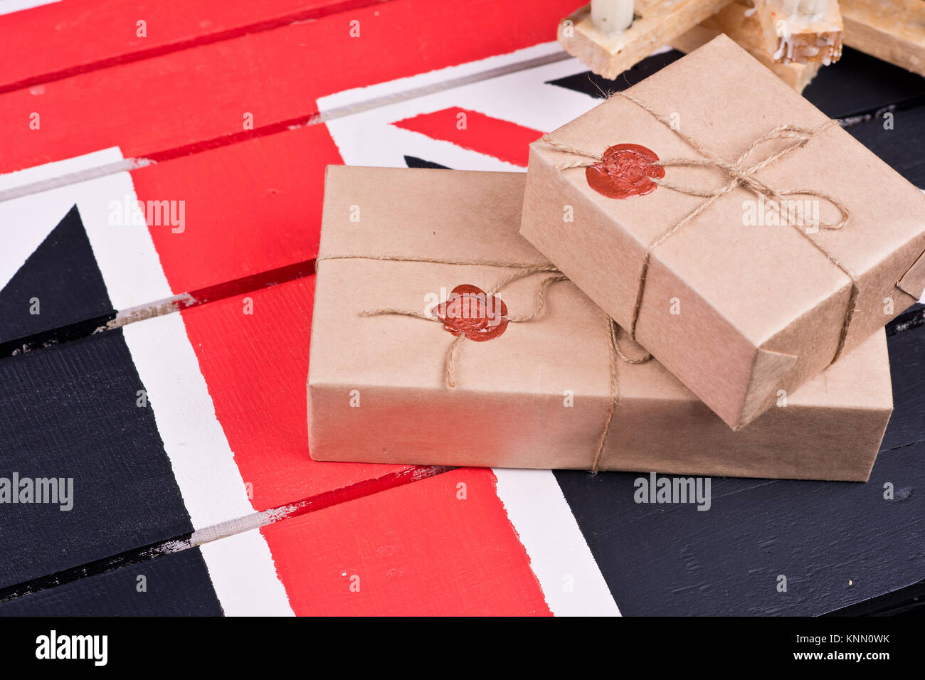 Boxen, eingewickelt in Handwerk Papier, mit packthread mit einem Wafer auf dem Hintergrund eines hölzernen Leuchter auf einem farbigen hölzernen Schreibtisch behoben. Stockfoto