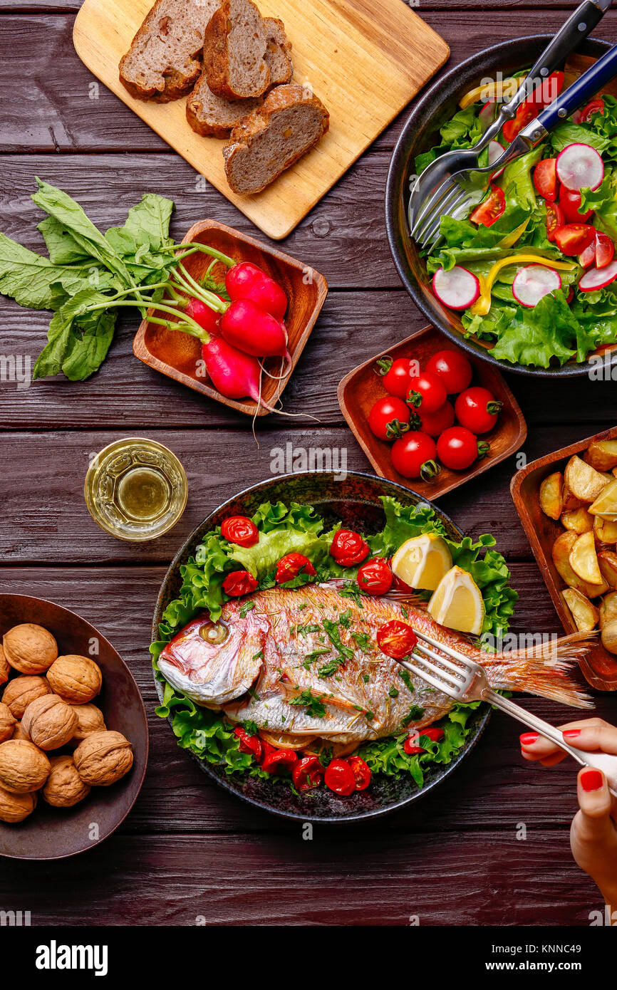 Frau essen gegrillter Fisch aus Tabelle mit farbenfrohen Speisen Stockfoto