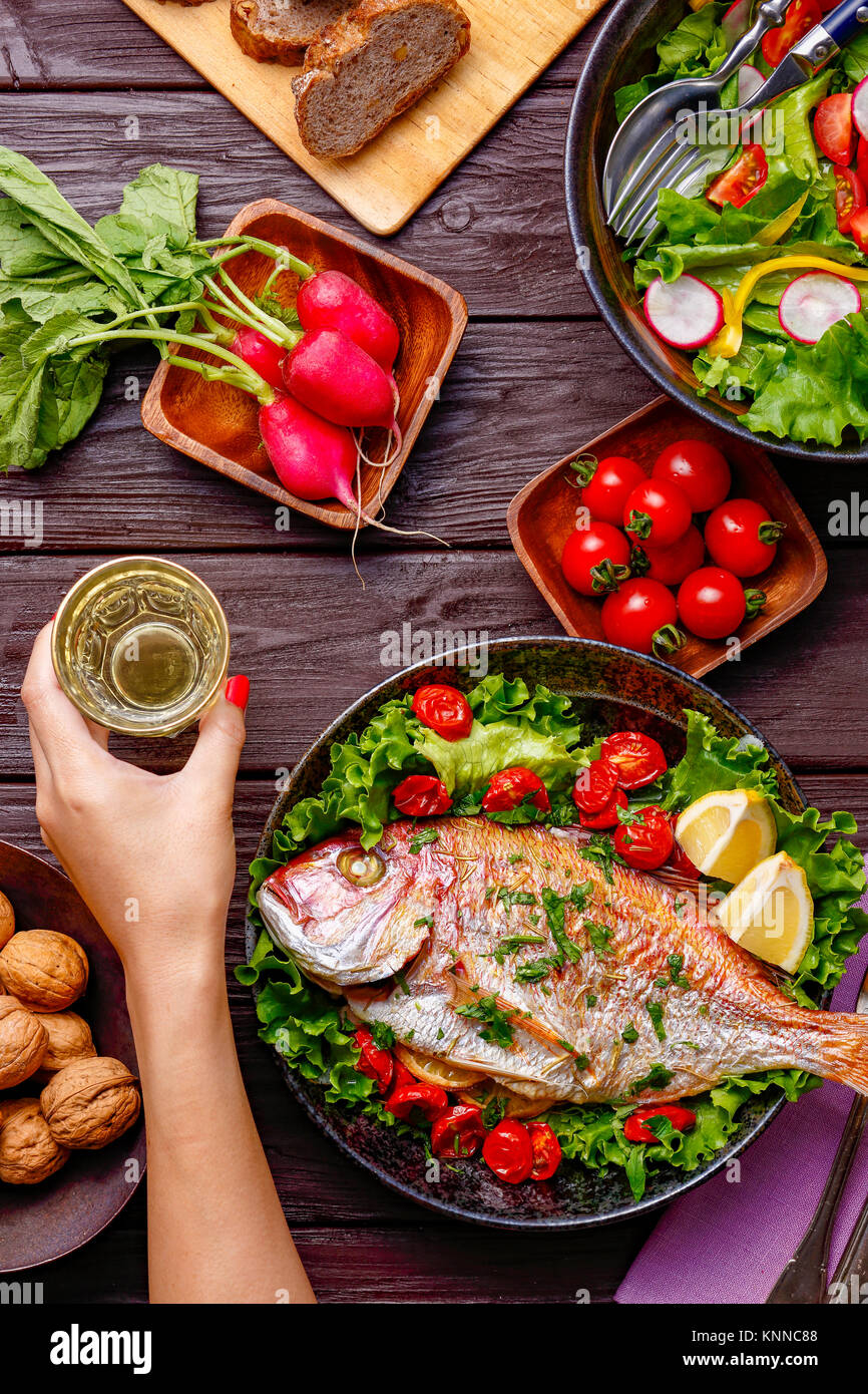 Frau Hand packte Wein aus Holztisch mit farbenfrohen Speisen Stockfoto
