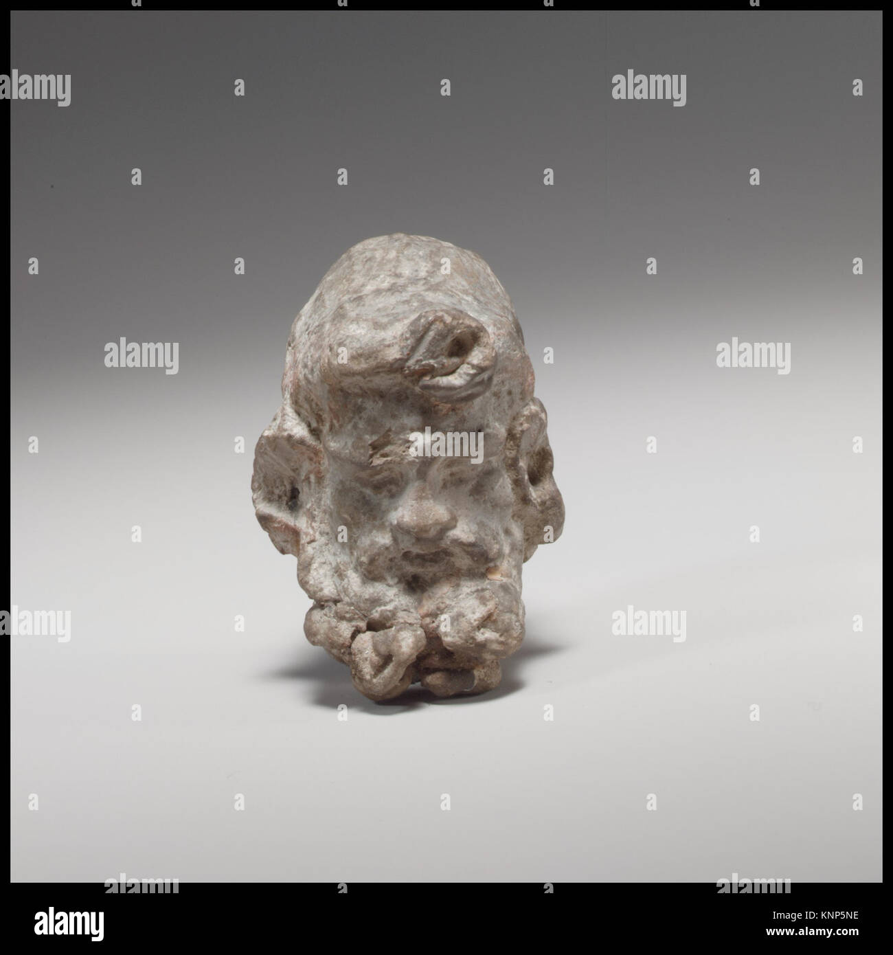 Ein geschnitzter Kopf eines Satyrs, der mythologische Merkmale wie spitze Ohren und ausdrucksstarke Gesichtsdetails zeigt, die als altes Artefakt erhalten sind. Stockfoto