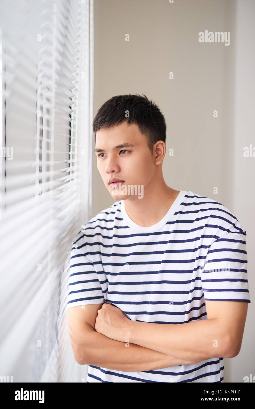 Porträt eines jungen Mannes mit gekreuzten Händen in der Nähe der Fenster. Stockfoto