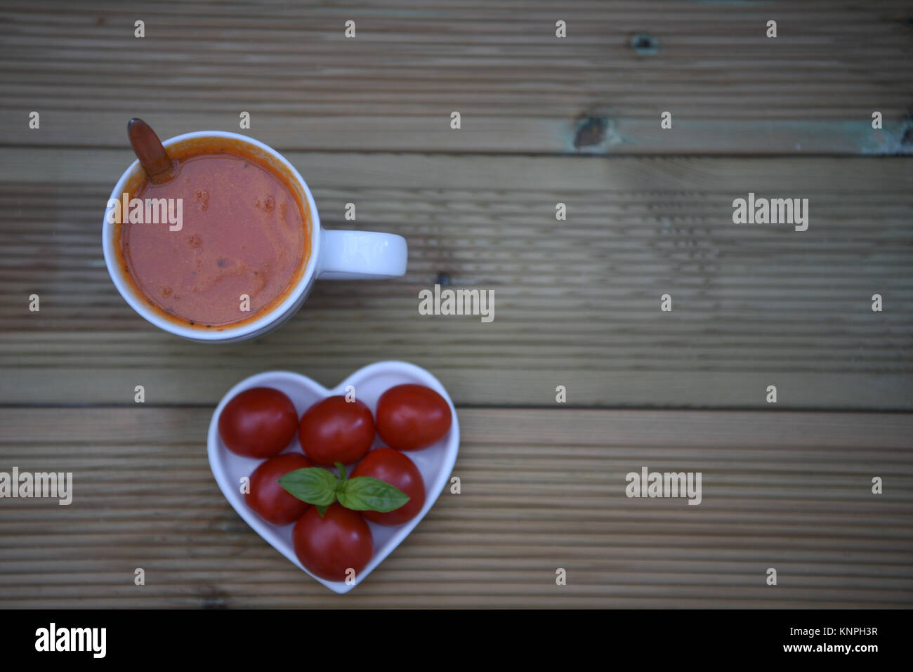 Essen Fotografie Bild von zu Hause aus Tomaten und Kräuter Suppe in einer Tasse mit Liebe Herzform Teller mit frischem Gemüse und Basilikum auf rustikalen, mit Holz gefüllt Stockfoto