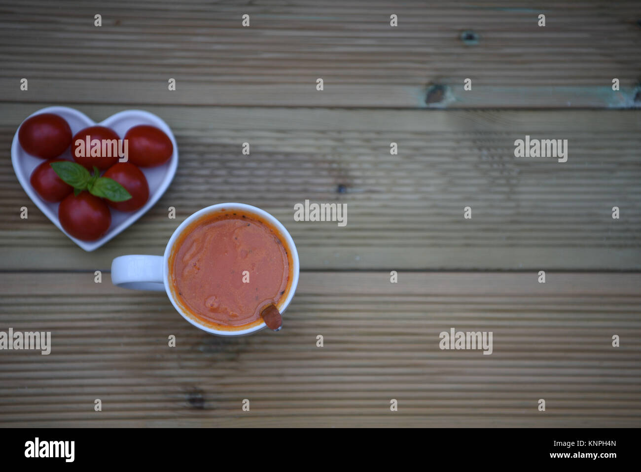 Essen Fotografie Bild von zu Hause aus Tomaten und Kräuter Suppe in einer Tasse mit Liebe Herzform Teller mit frischem Gemüse und Basilikum auf rustikalen, mit Holz gefüllt Stockfoto