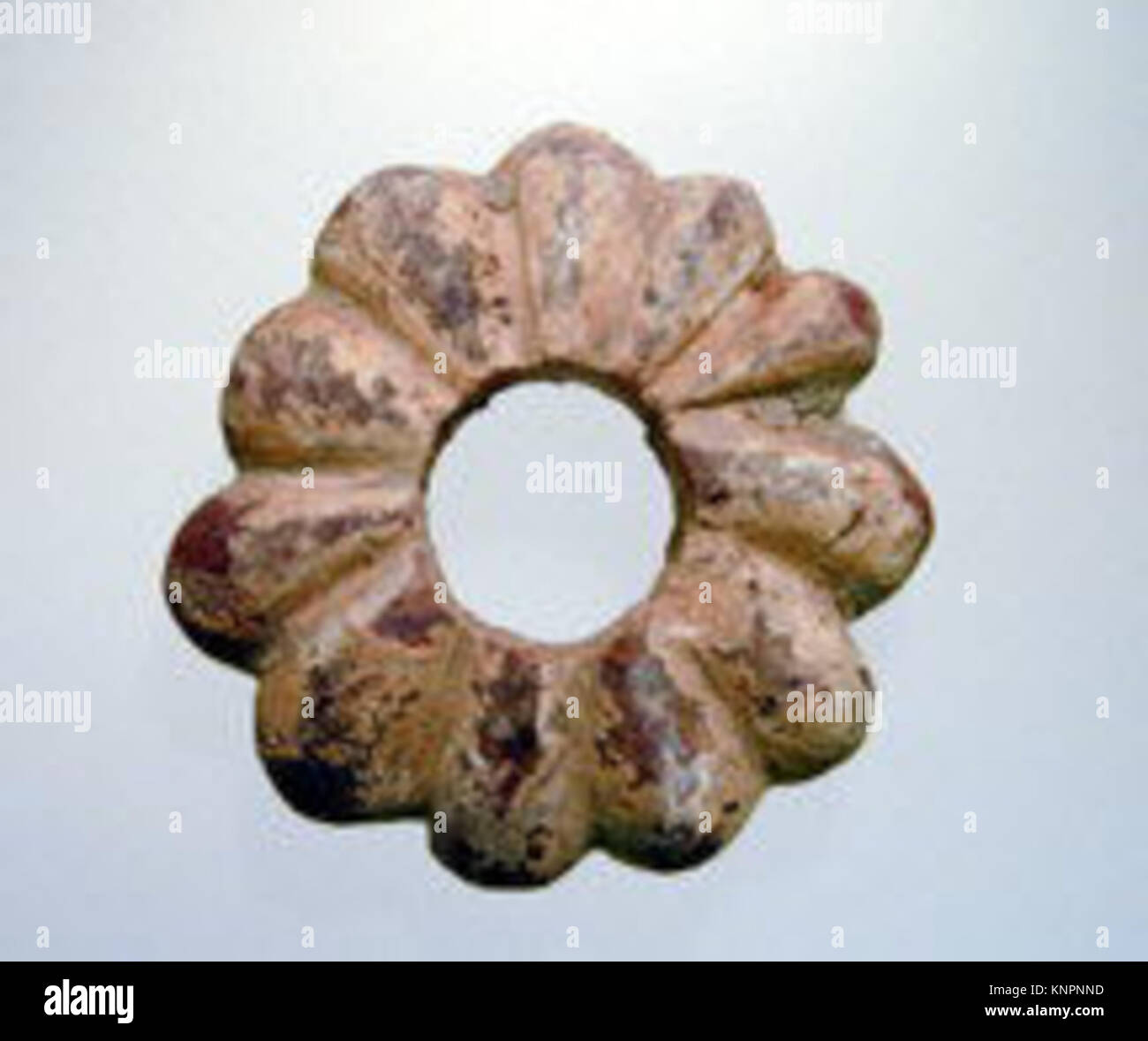 Eine antike, blumenförmige Perle aus Halbedelmaterial mit mehreren im Relief geschnitzten Blütenblättern. Wird wahrscheinlich als dekoratives Element in Schmuck oder Kleidungsstücken verwendet. Stockfoto