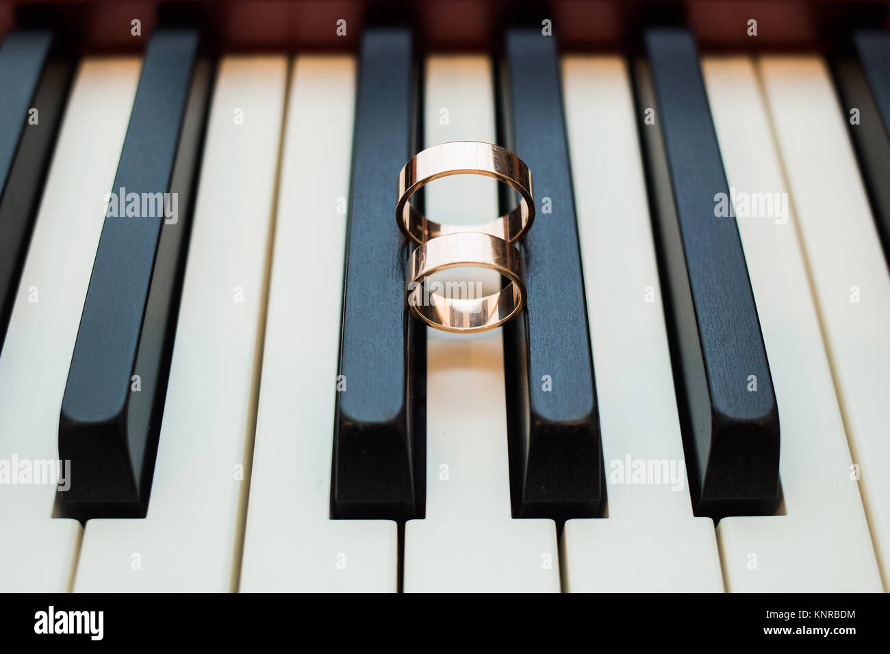 Zwei schöne glänzende Hochzeit goldene Ringe an den schwarzen und weißen Tasten des Klaviers. Horizontale Farbfotografie. Stockfoto