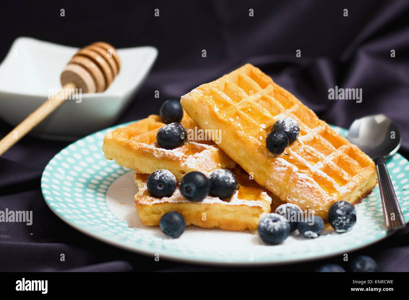 Stacke von mehreren Rechteck Waffeln mit Honig, Blaubeeren und Puderzucker zum Essen als Frühstück oder ein Snack serviert. Stockfoto