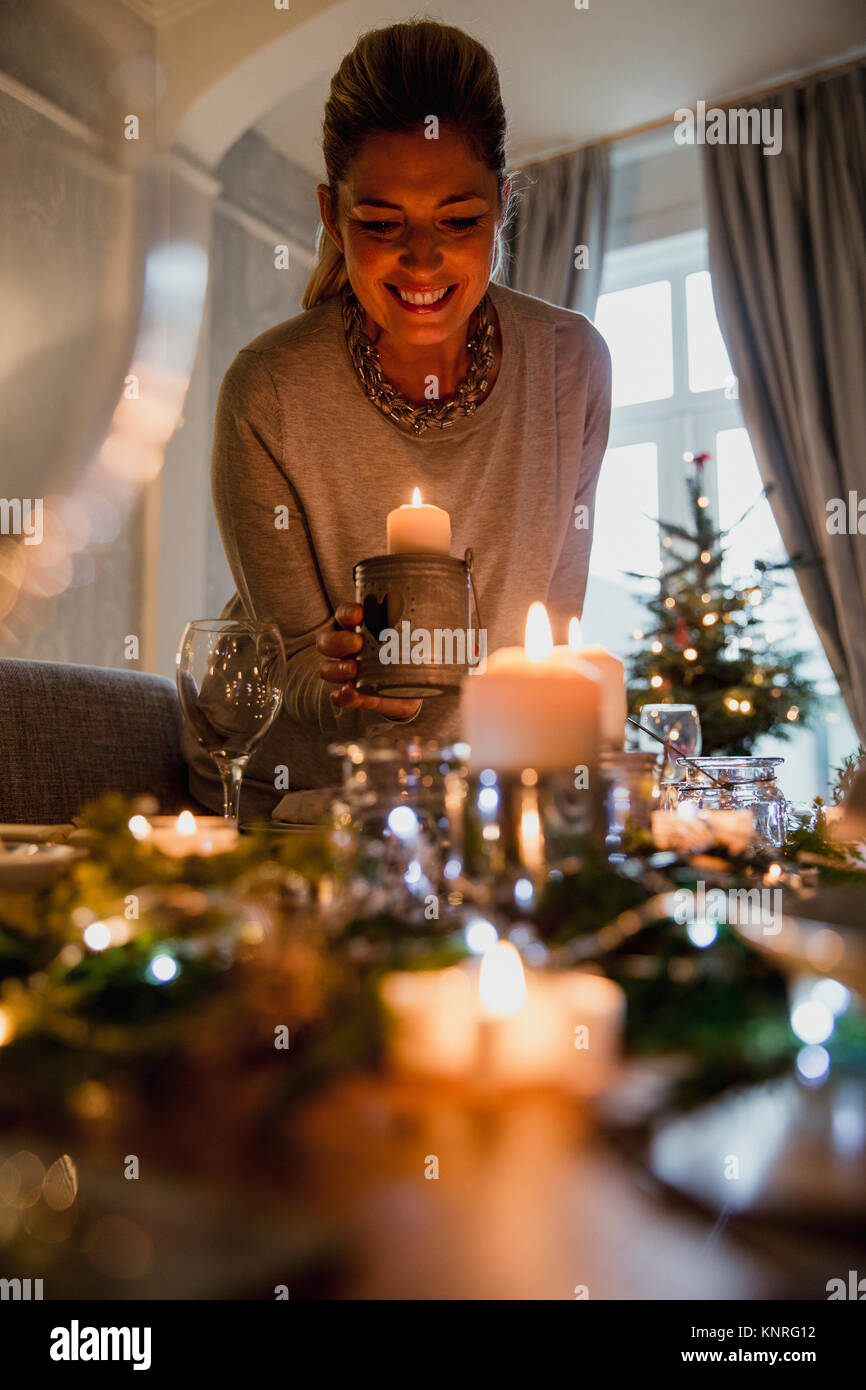Glückliche Mutter ist die Einstellung der Tabelle für Weihnachten Abendessen mit Ihrer Familie. Sie ist Kerzen anzünden. Stockfoto