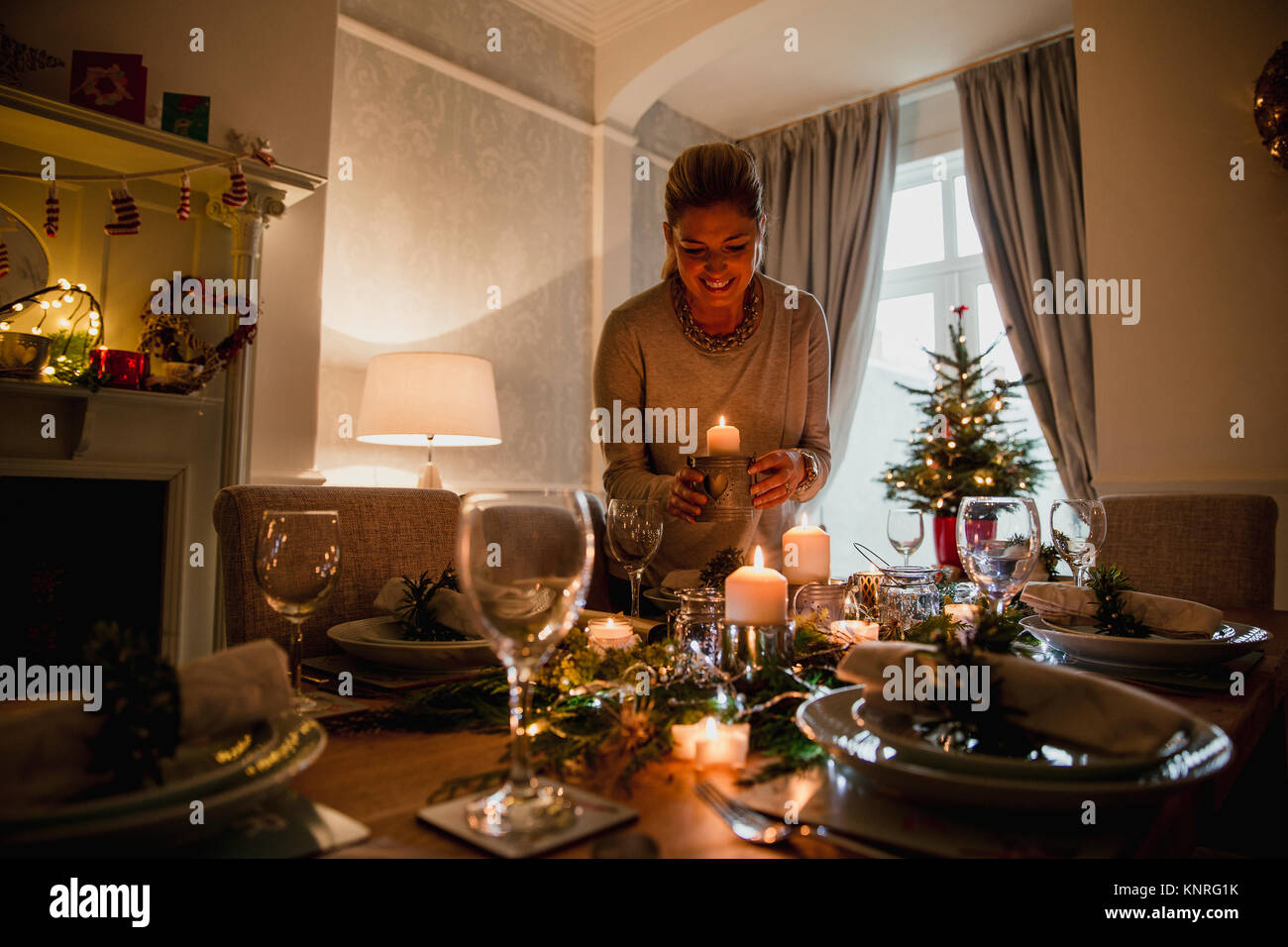 Glückliche Mutter ist die Einstellung der Tabelle für Weihnachten Abendessen mit Ihrer Familie. Sie ist Kerzen anzünden. Stockfoto