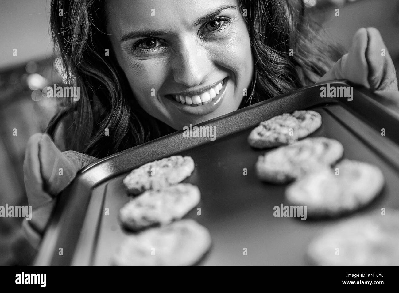 Glückliche junge Hausfrau zeigt Pfanne mit Weihnachtsgebäck Stockfoto