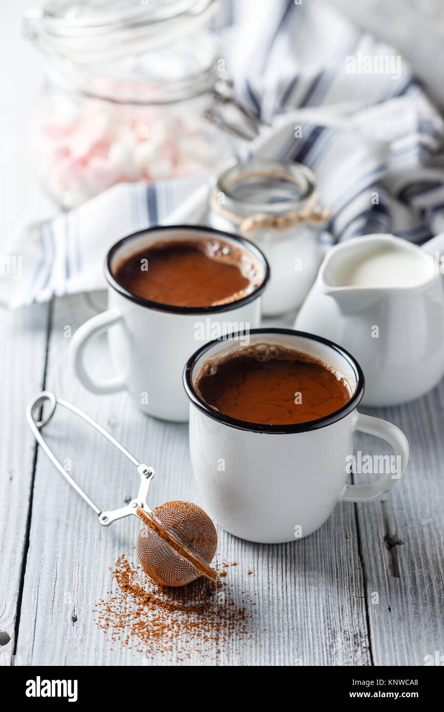 Heißer Kakao in zwei emaillierten weiße Tassen auf hellem Holztisch. Stockfoto