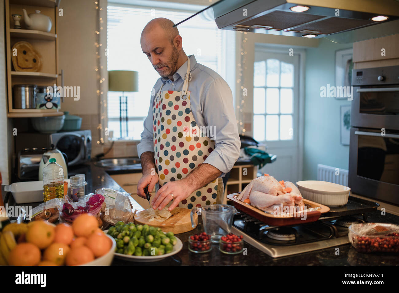 Ein reifer Mann bereitet ein Weihnachtsessen in der Küche seiner Wohnung. Er ist Kartoffeln schälen. Stockfoto