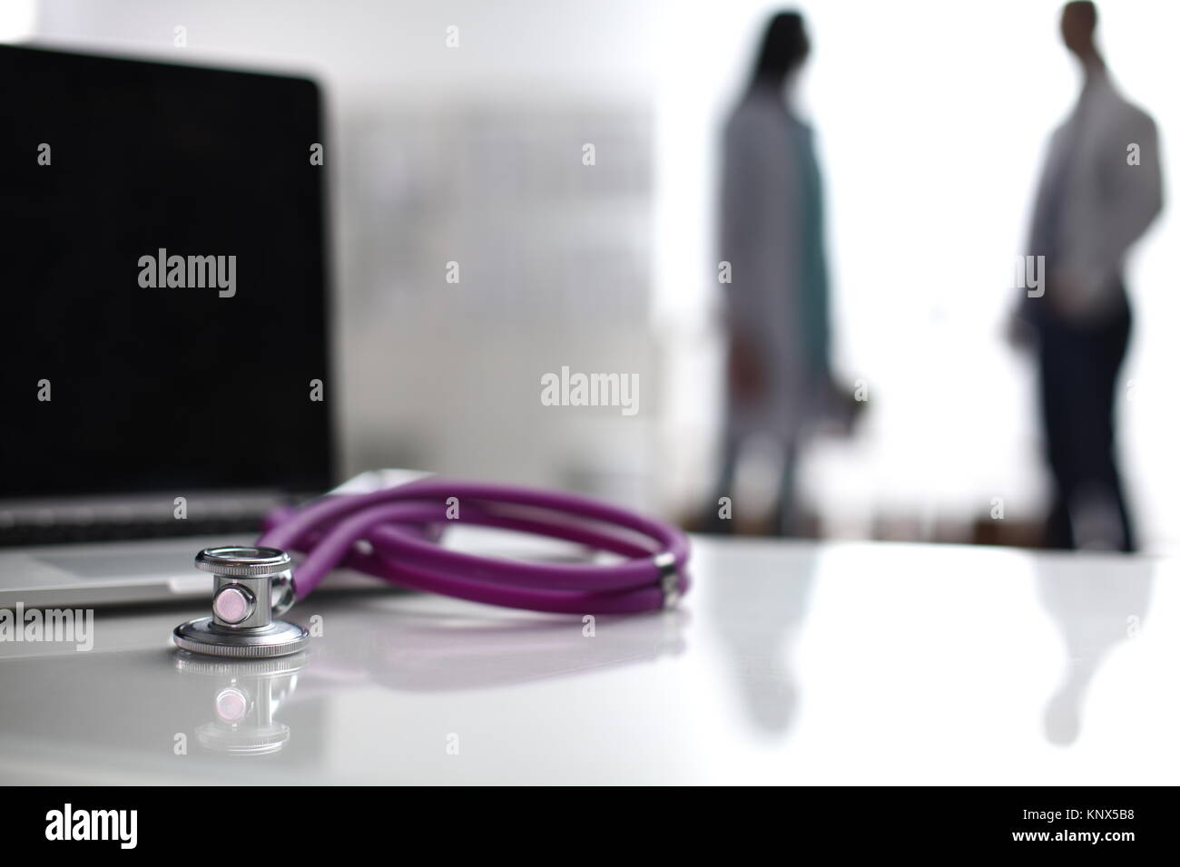 Laptop und medizinische Stethoskop auf dem Schreibtisch, Ärzte im Hintergrund stehend Stockfoto