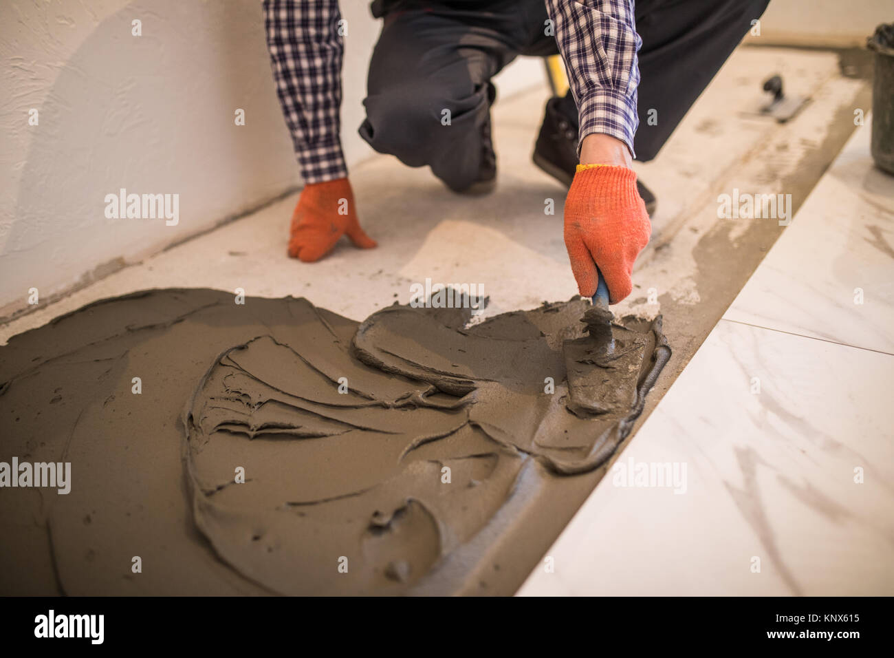 Troweling Mörtel auf Betonboden in der Vorbereitung für die Verlegung von weißen Bodenfliesen. Stockfoto