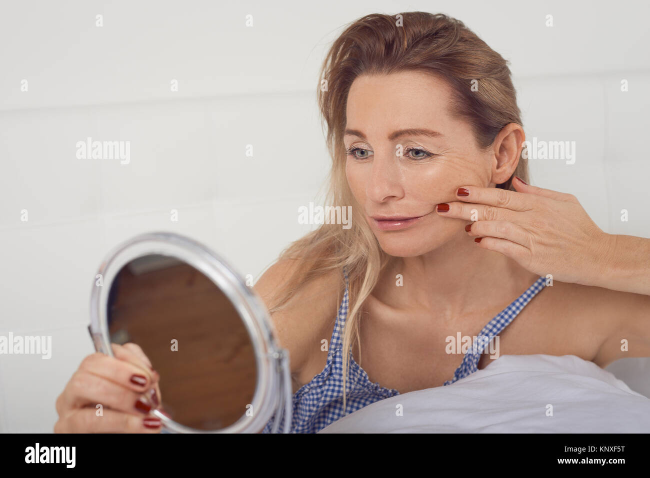 Porträt von einem besorgten Frau denken des Alterns während in den Spiegel an ihr Gesicht und ihr Gesicht Falten Stockfoto
